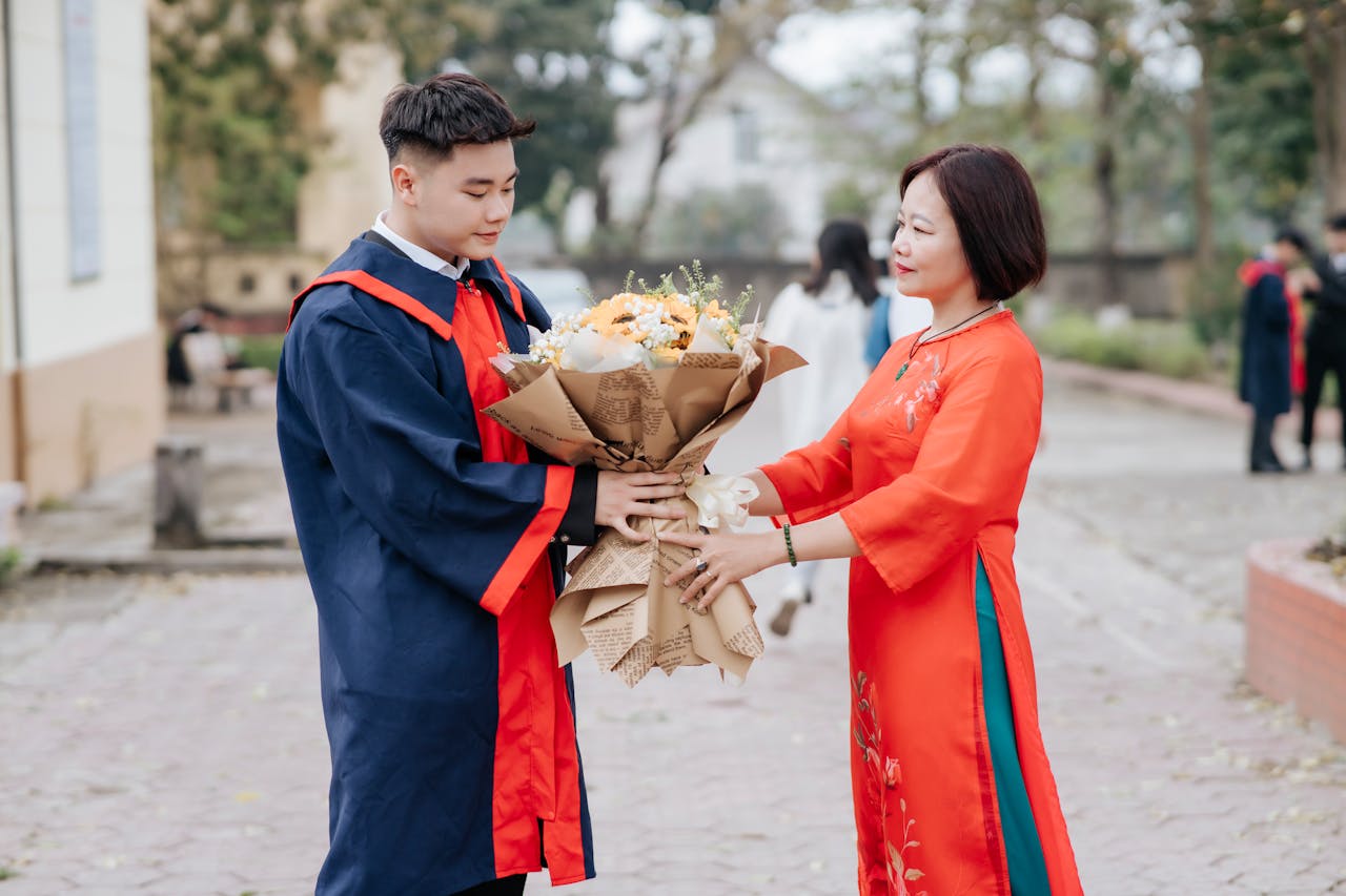 Young graduate receiving a congratulatory bouquet from a family member outdoors.